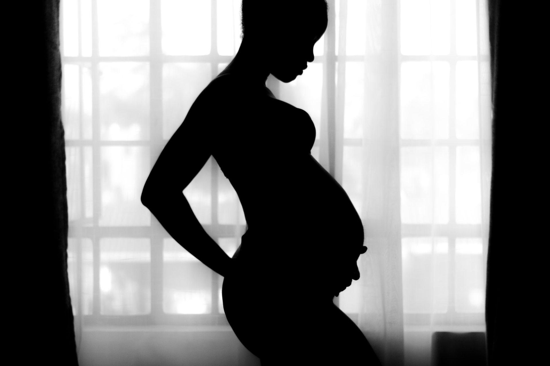 Black and white photo of pregnant woman holding her back with on hand and her belly with the other