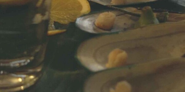 Mussel shells, a lemon wedge and a full glass on a table top.