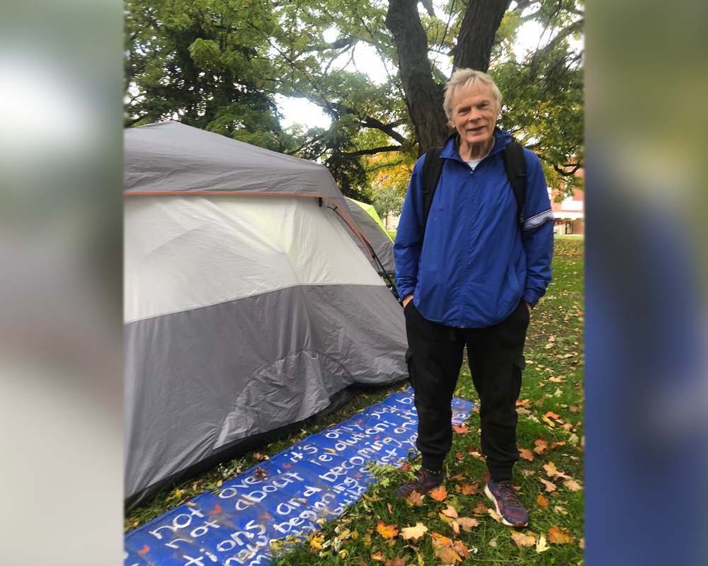 Phil, an encampment resident at Allan Gardens Park, stands next to a sign behind his tent which reads “It is not over, it’s only just beginning. It’s not about revolution, it’s about solutions and becoming one again. It’s a new beginning. Start your own community, build your own home.”