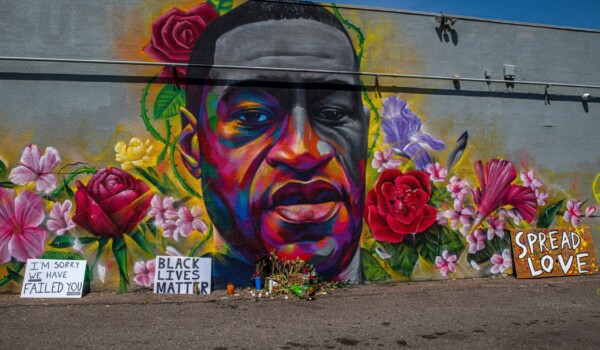 A mural of a man's face surrounded by colourful flowers on a grey concrete background