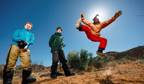 The three members of black midi are dressed in hiking gear in the desert