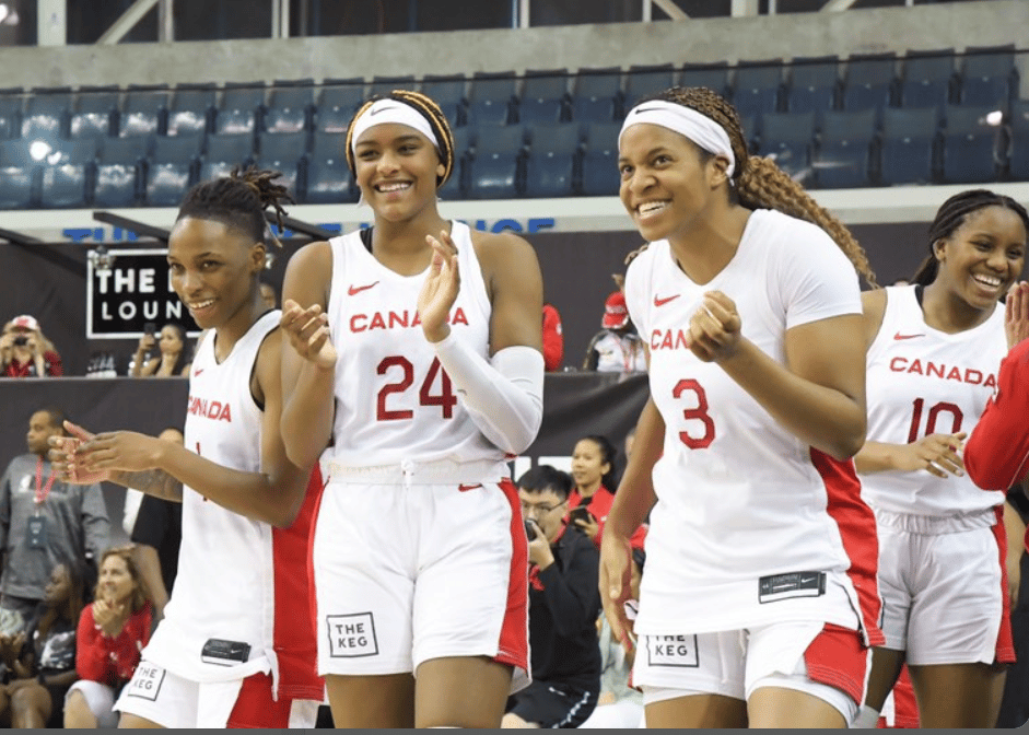 People in basketball uniforms are smiling as they stand on a court.