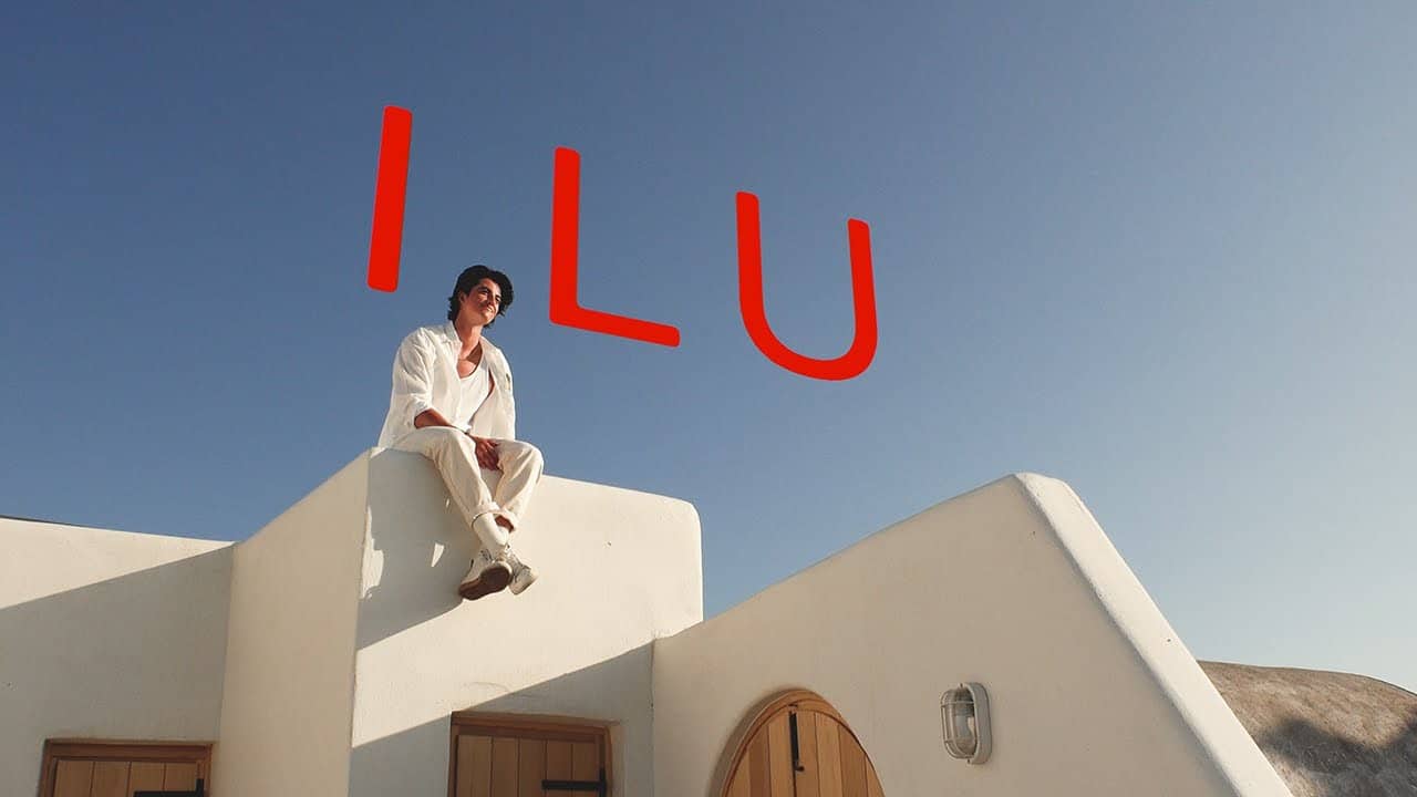 Elijah Woods is sitting on a greek-style house, with the letters "ILU" in the sky above him